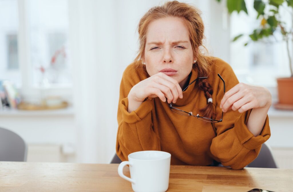 A person squinting their eyes while holding their glasses.