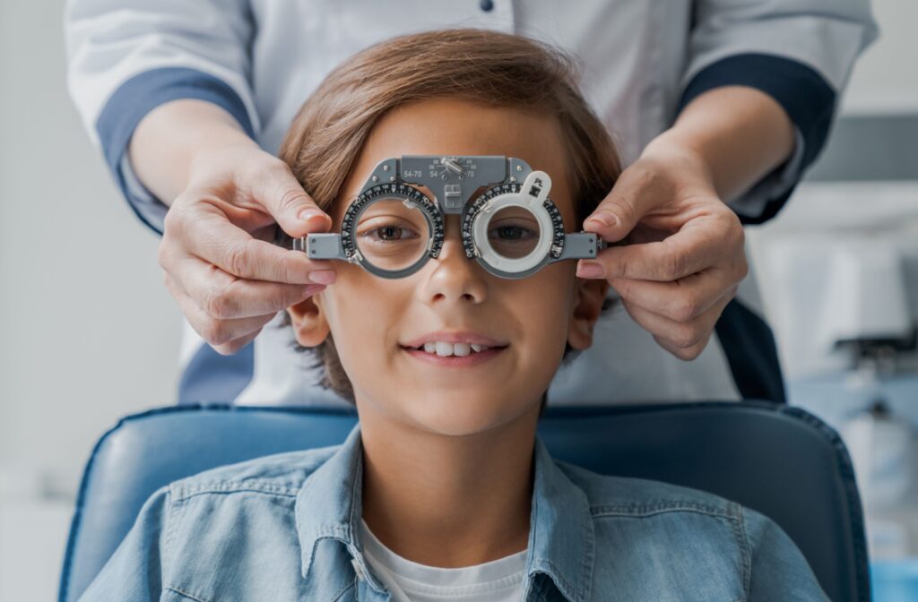 A child sits in an eye exam chair while a professional adjusts trial frames for accurate vision testing