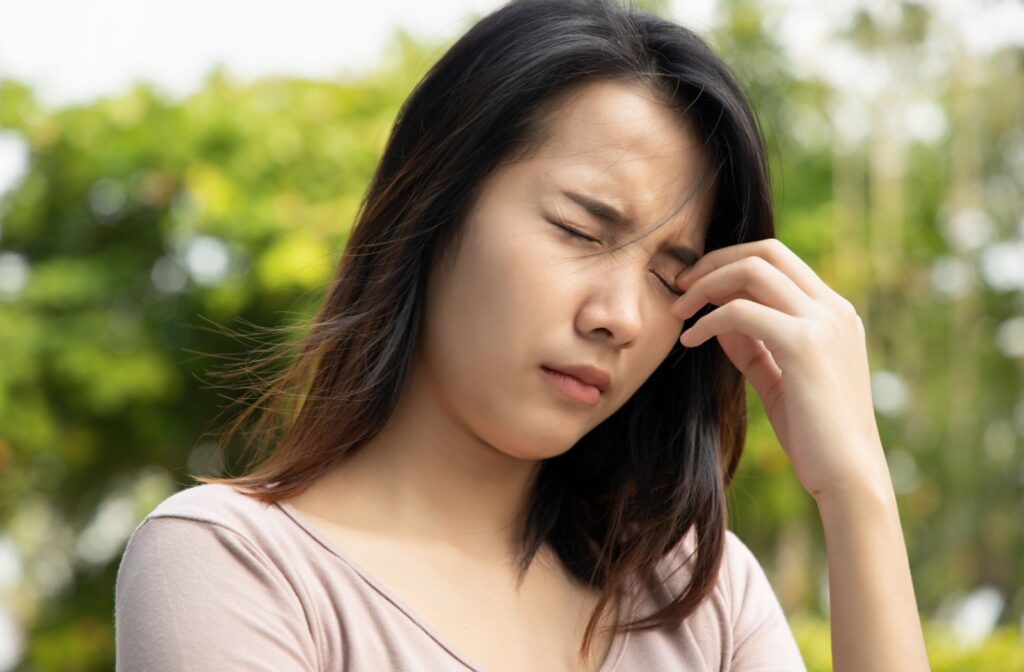 A young adult rubbing their eyes in discomfort while walking outside due to dry eye irritation.