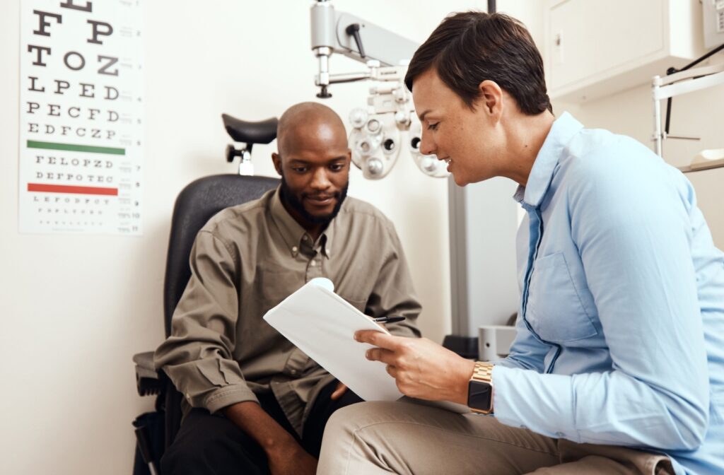 A smiling optometrist showing a patient a clipboard after an eye exam to find the cause of their dry eye.