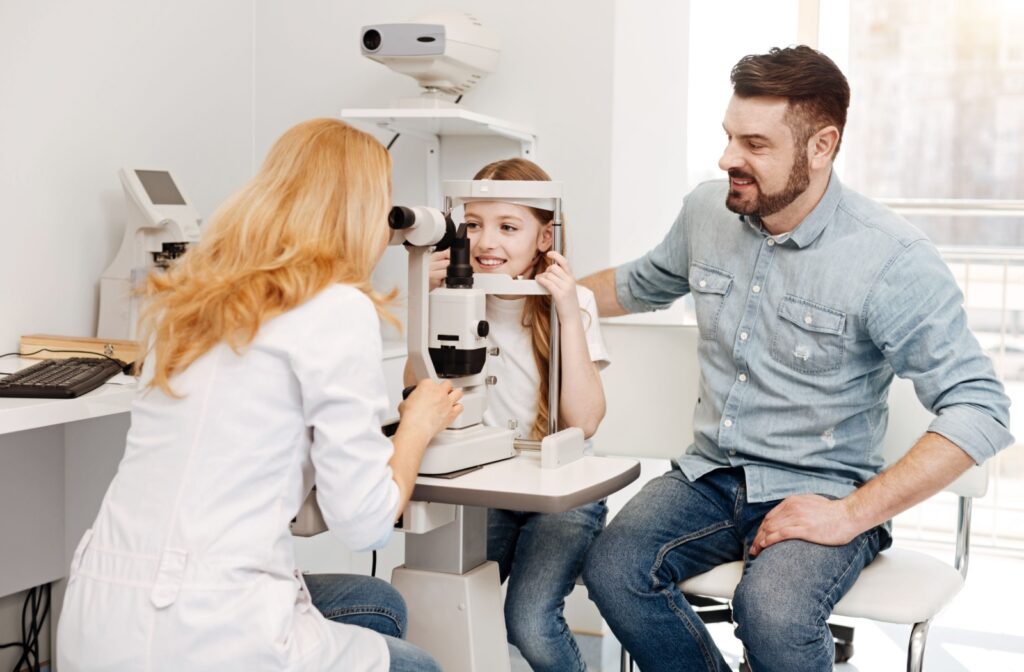 An eye doctor performing an eye exam on a school-aged child with their parent present.