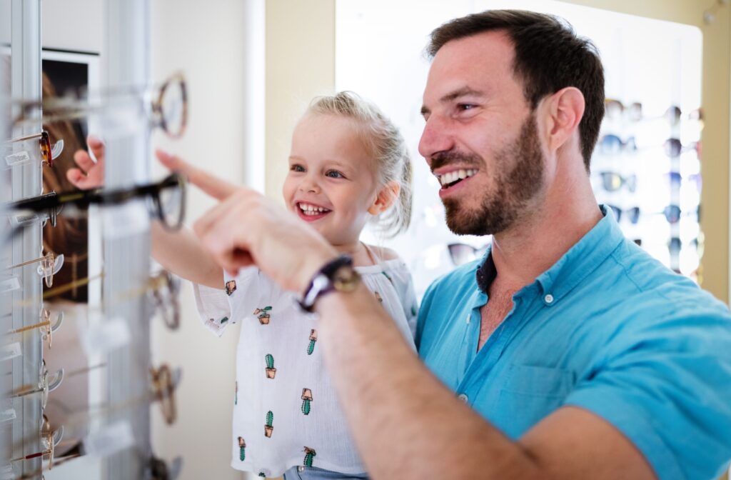 A parent and their young child happily picking out new glasses at an optometry clinic.