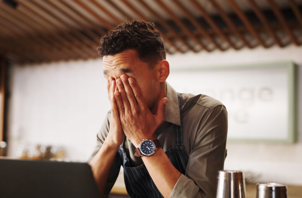 Person sitting at a desk covering tired eyes with both hands from eye strain