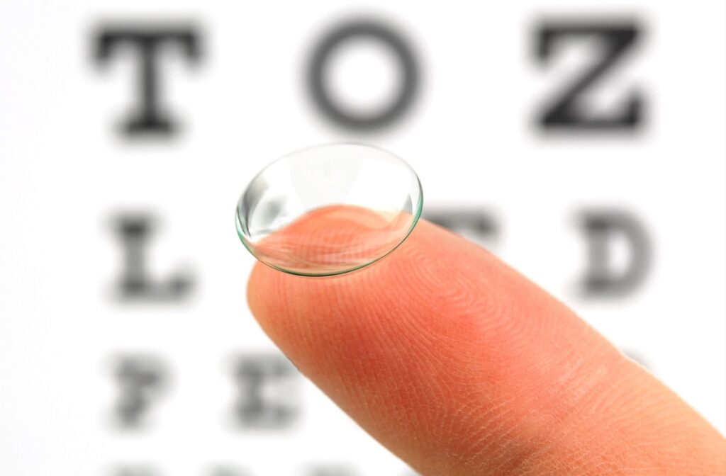 A contact lens sits on a finger in front of an eye chart.