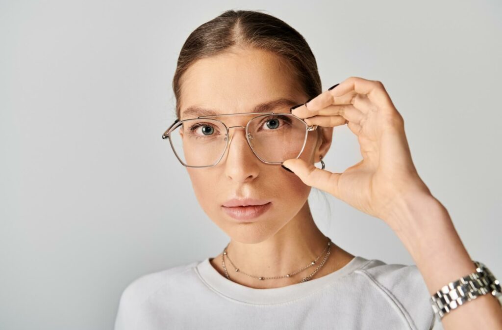 Close-up of a stylish person looking directly into the camera and adjusting their silver, aviator-style glasses.