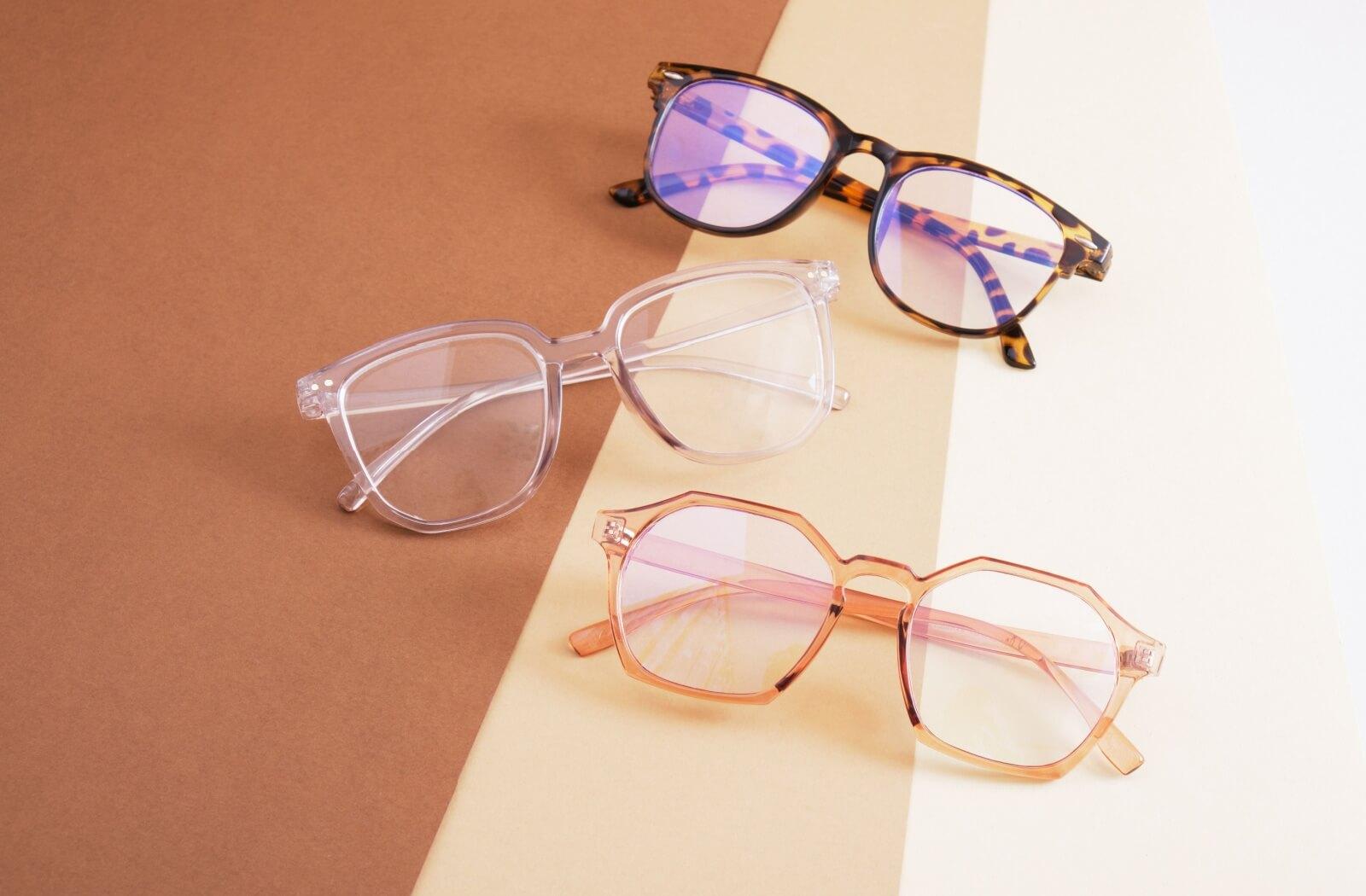 Flatlay of 3 pairs of stylish eyeglasses in tortoiseshell, clear, and pink translucent frames.